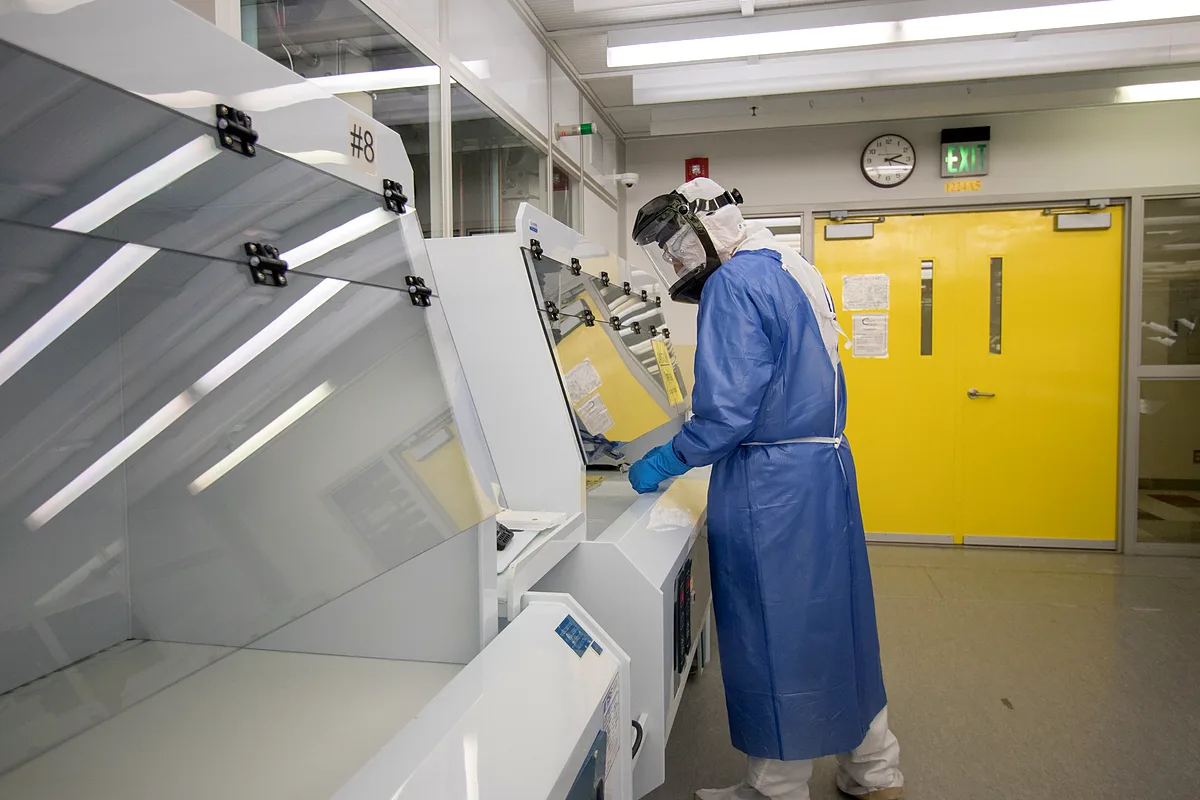 Engineer in blue gown, face shield and nitrile gloves at a cleanroom wet bench
