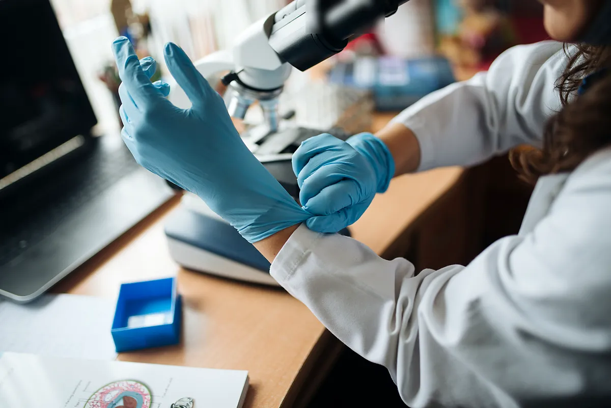 Laboratory worker pulling on blue nitrile gloves at a microscope