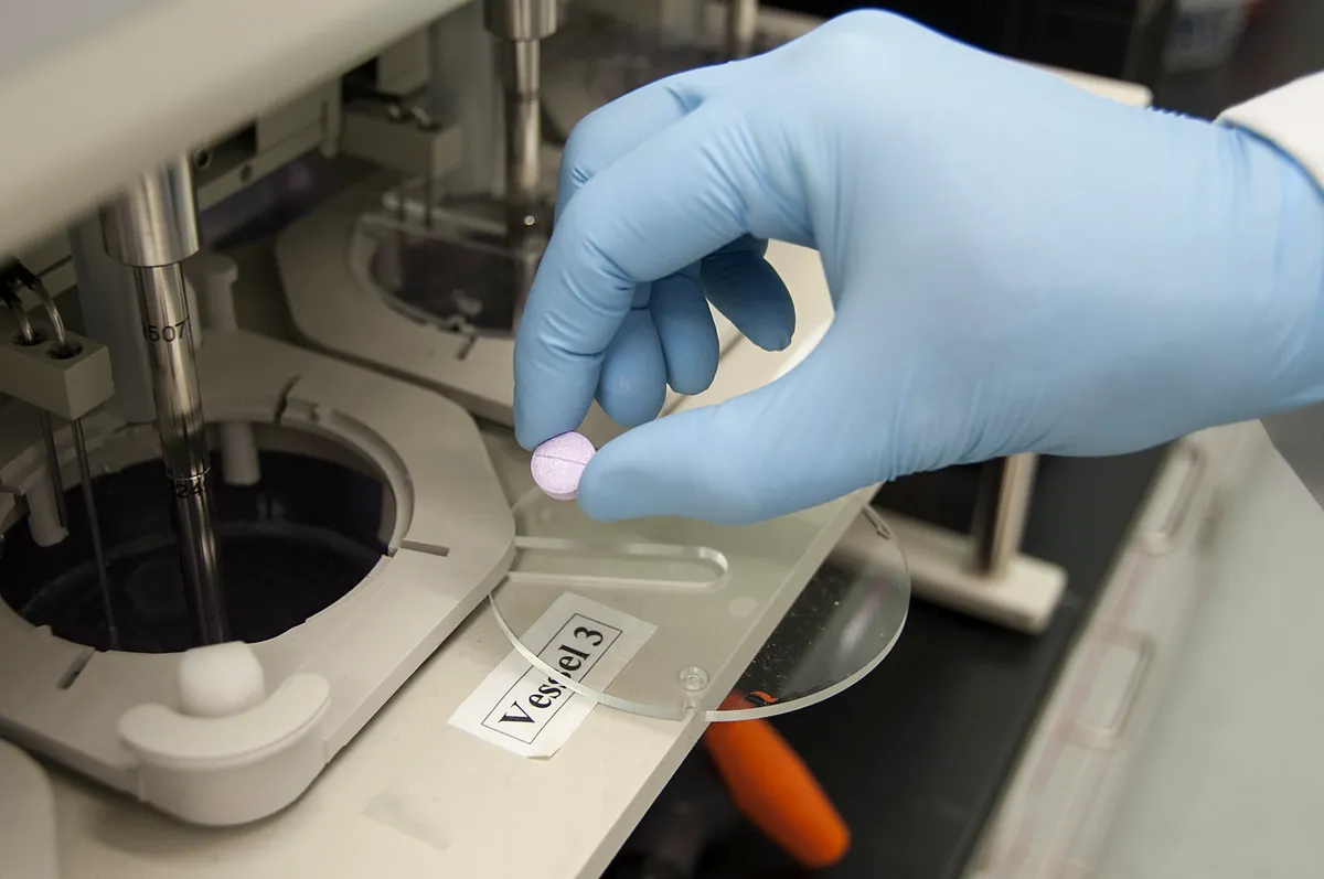 Gloved hand placing a tablet into a dissolution test vessel