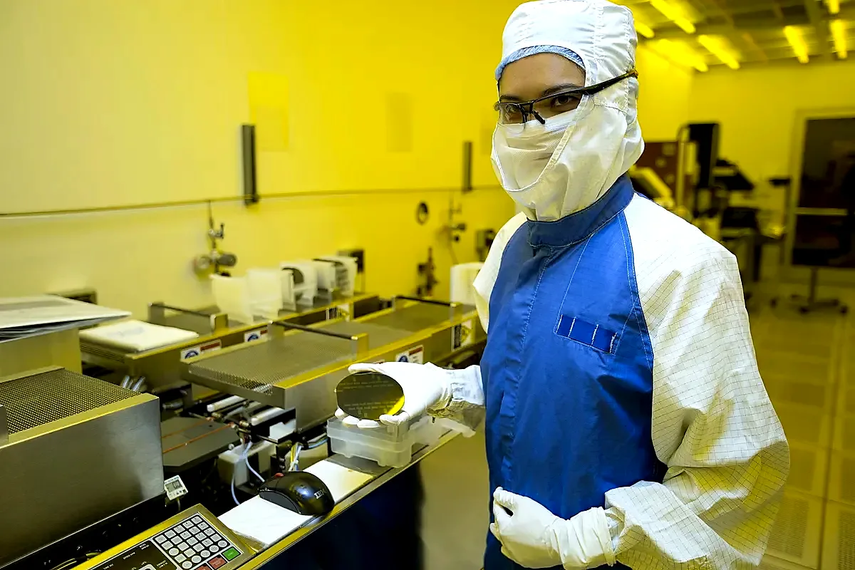 Gowned operator in mask and gloves holding a silicon wafer